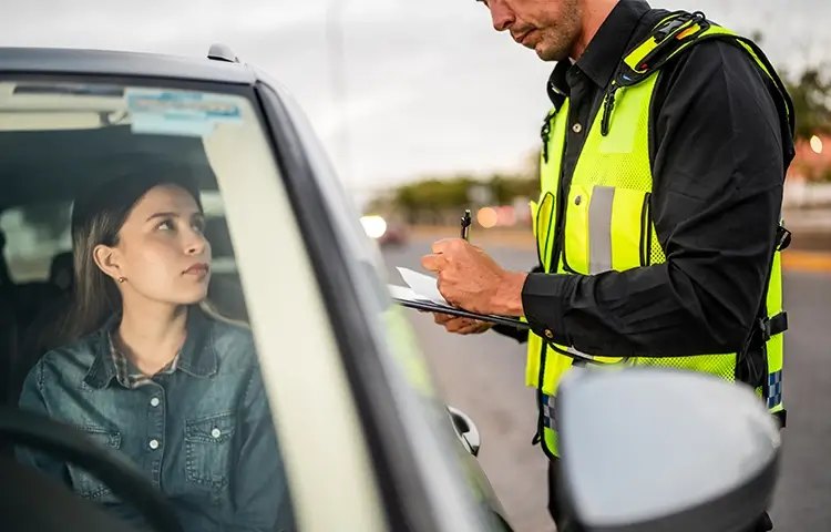 Agente de trânsito preenchendo uma autuação ao lado de uma motorista parada